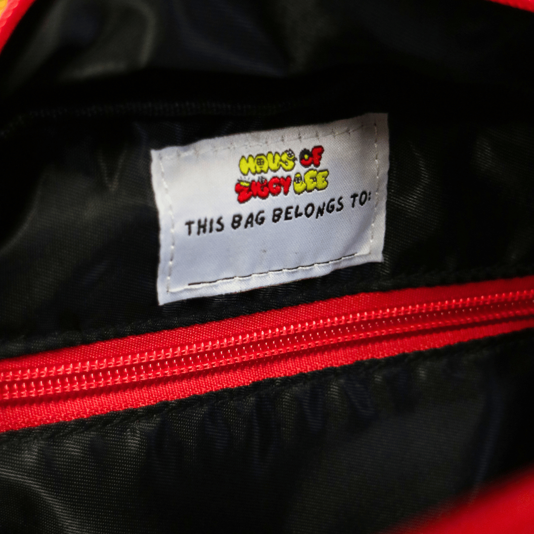 Close-up of the interior of haus of ziggy lee everyday deadly backpack showing a white sewn-in embroidered label that reads 'Haus of Ziggy Lee' and 'THIS BAG BELONGS TO:'.